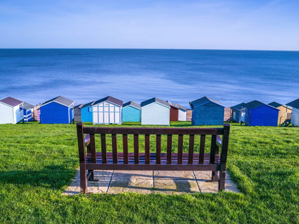 Picture of BENCH ON LAWN WITH BEACH HUTS IN BACKGROUND