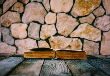 Picture of OLD OPEN BOOK ON OLD WOODEN TABLE ON A BACKGROUND OF STONE WALLS