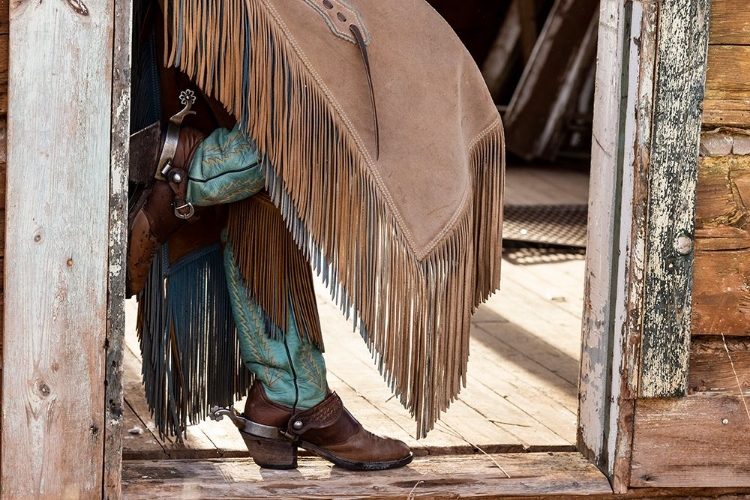 Picture of USA- SHELL- WYOMING. HIDEOUT RANCH COWGIRL STANDING IN DOORWAY WITH COWBOY BOOTS AND CHAPS. 